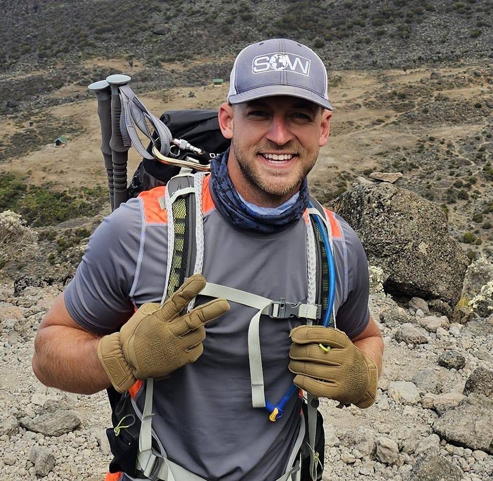 Tyler Woodall hiking up Mount Kilimanjaro wearing a SOW Project cap